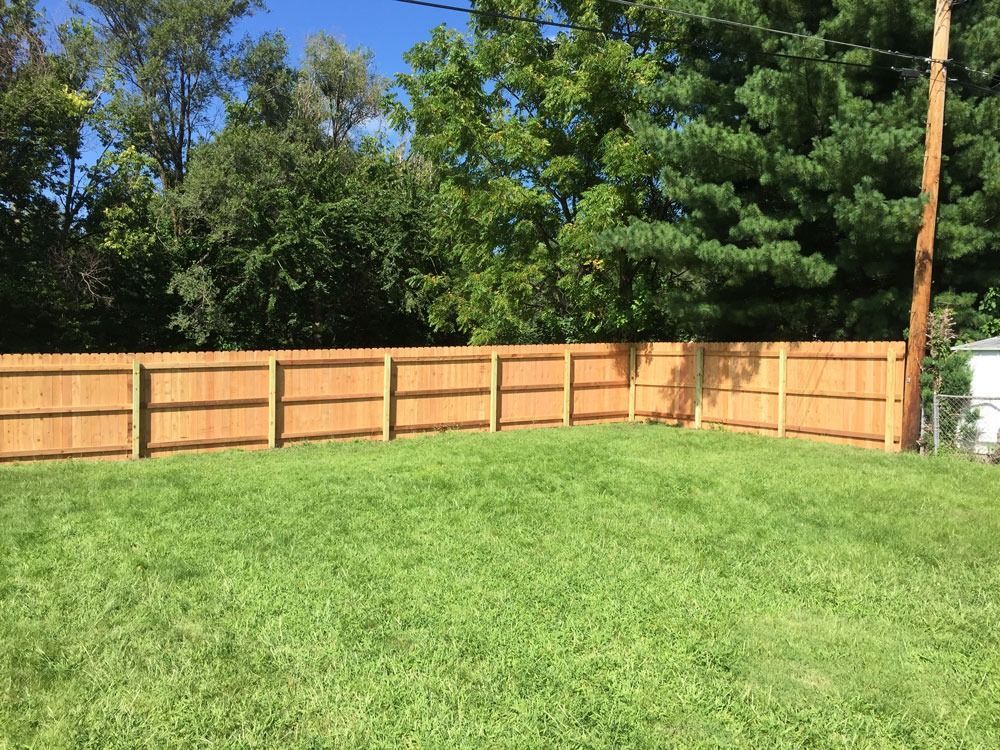 Wooden fence encloses a green lawn, trees in background, sunny day.