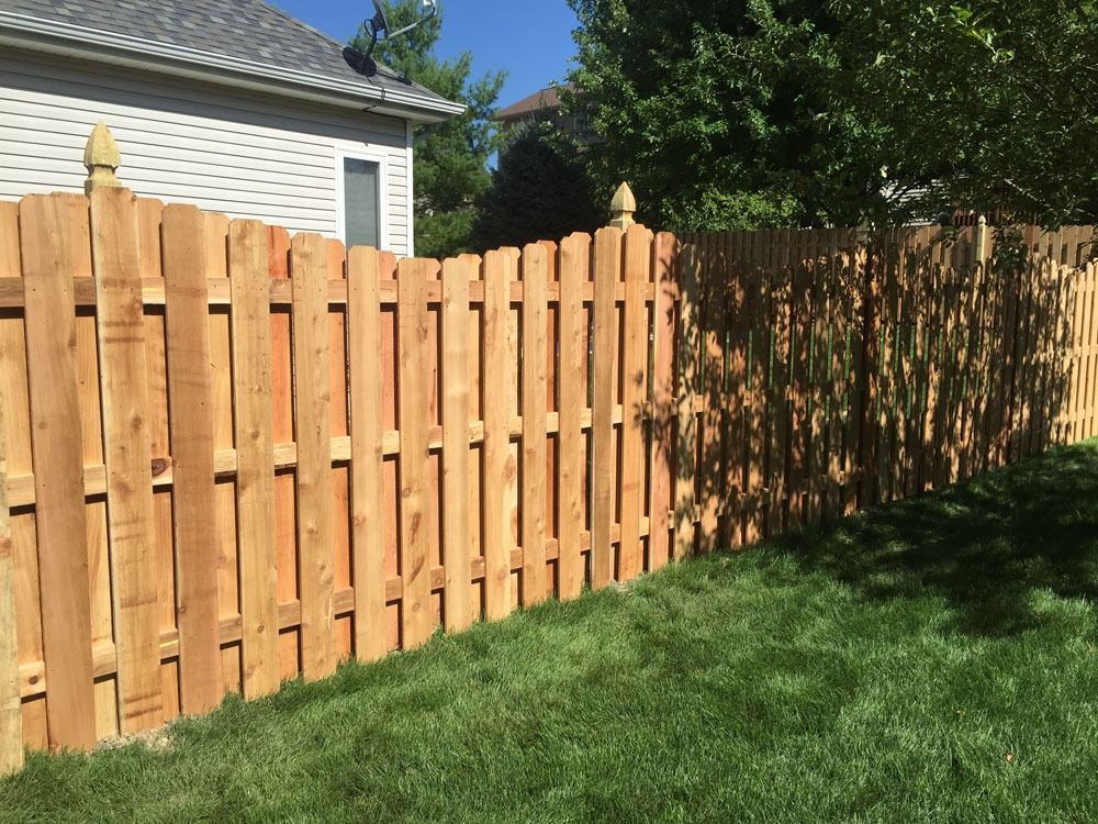 Wooden fence in a backyard with green grass, and a house in the background.
