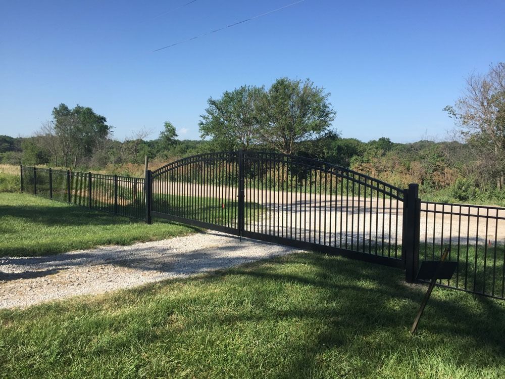 Black metal gate on gravel driveway leading into a field.