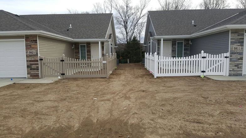 Two attached houses with picket fences and a dirt path between them.