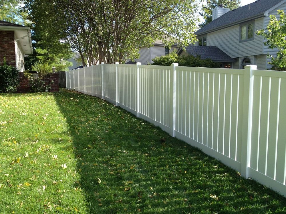 White vinyl fence in a grassy yard, separating two suburban homes.