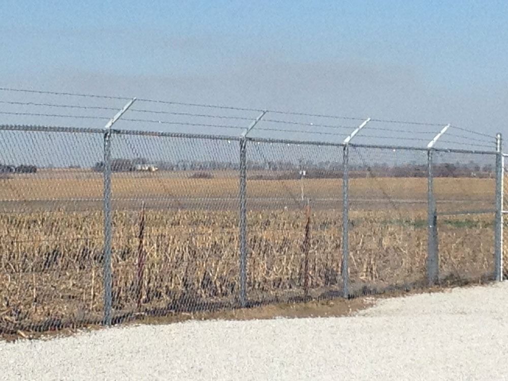 Chain link fence with barbed wire on top, enclosing a field.