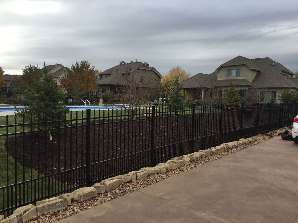 Black metal fence surrounding a yard with a pool. Houses are in the background, overcast sky.