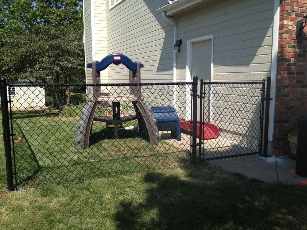 Black chain-link fence encloses a small backyard play area with a slide set against a house.