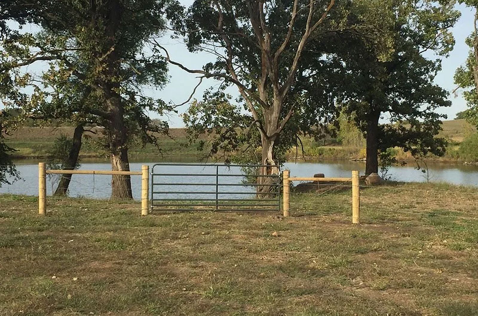 Fence with gate in front of a lake, trees in the background.