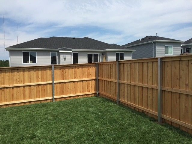 Wooden fence enclosing a grassy backyard, with a light gray house in the background. Blue sky overhead.