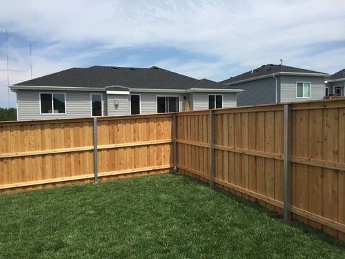 Wooden fence enclosing a grassy backyard, with a light gray house in the background. Blue sky overhead.