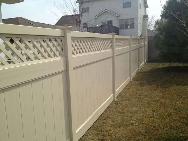 Beige vinyl fence with lattice top in a grassy backyard.
