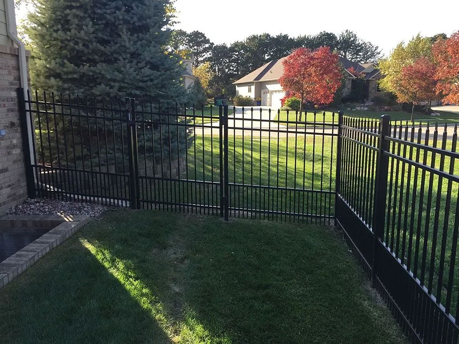 Black metal fence enclosing a grassy yard, house and trees in background.