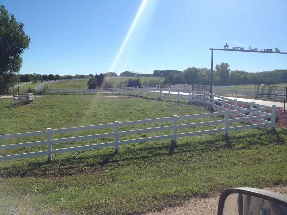 White fence around a grassy field with an archway entrance on a sunny day.