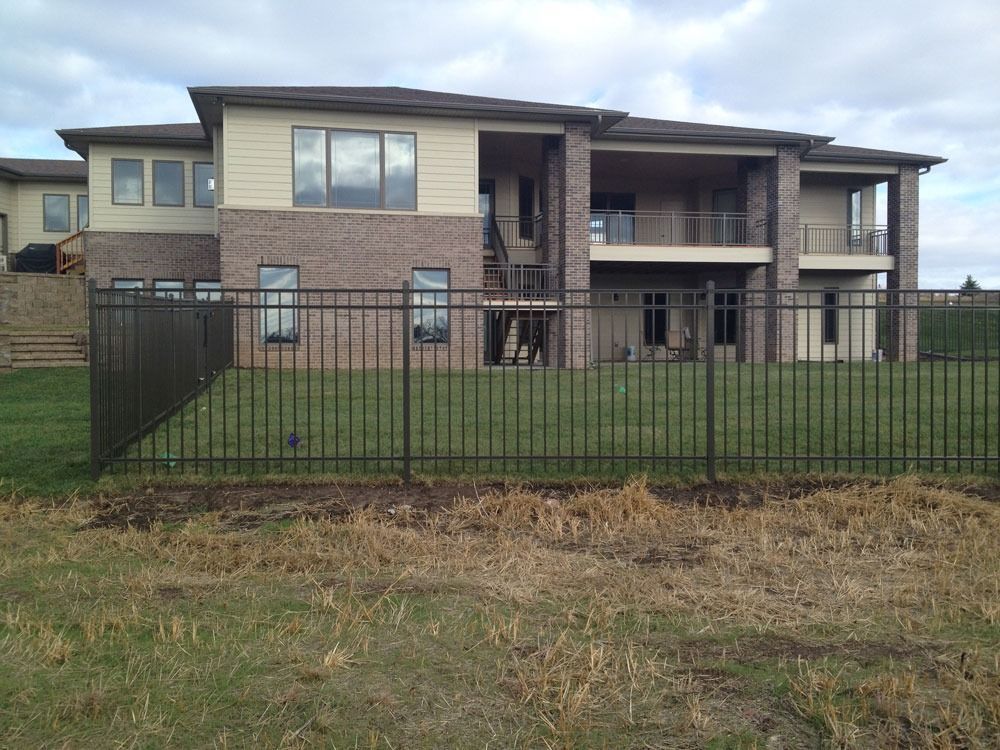 Black metal fence in front of a two-story house with brick and beige siding. Overcast sky.