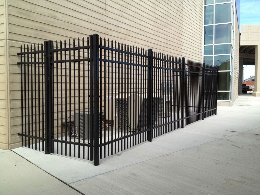 Black metal fence encloses equipment next to a building with glass windows.