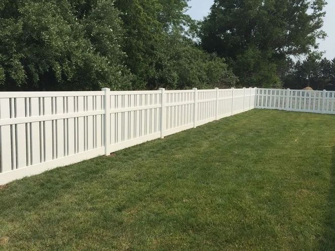 White vinyl fence surrounding a green grassy yard, with trees in the background.