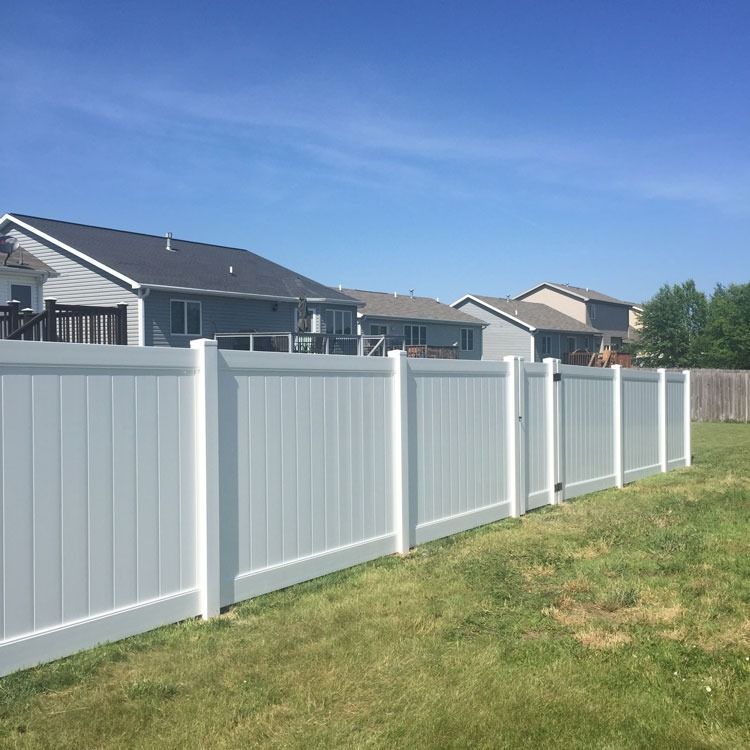White vinyl fence in a grassy backyard, houses in the background under a blue sky.