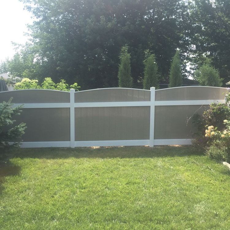 White framed fence with a wavy top and brown panels, set on a grassy lawn.