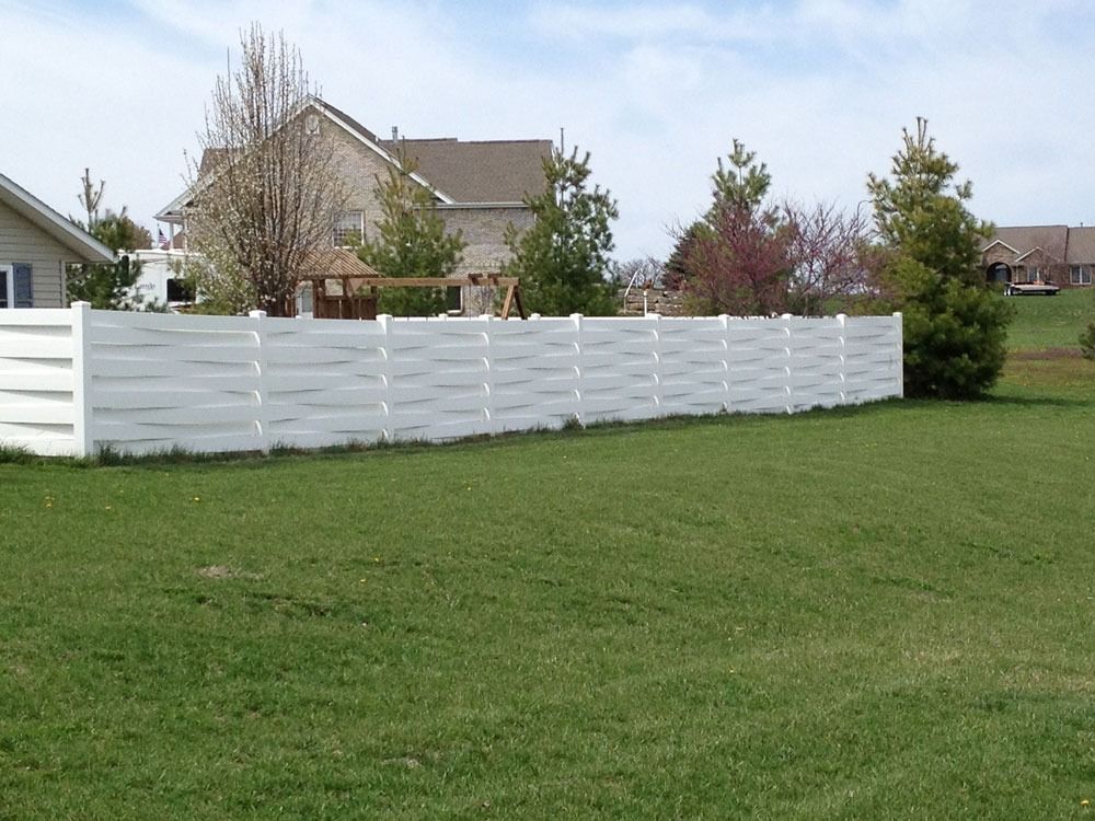 White vinyl fence in a grassy backyard, houses in the background under a blue sky.