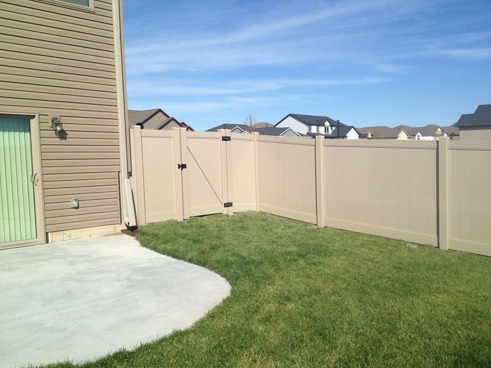 Tan vinyl fence encloses a small, grassy backyard next to a light-colored house.