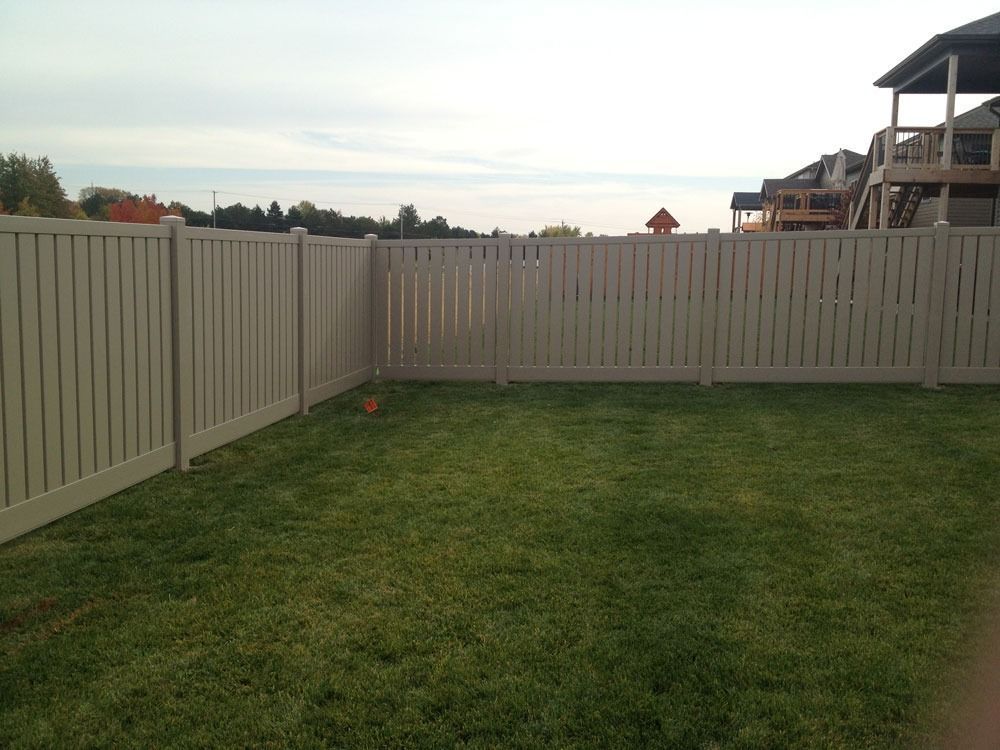 A beige vinyl fence encloses a green lawn. Cloudy sky, buildings in the background.