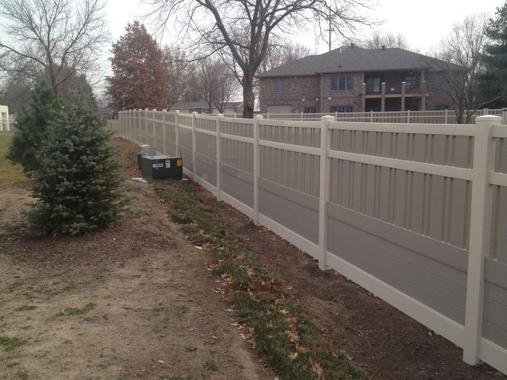 Tan and white vinyl fence bordering a residential property on a cloudy day.