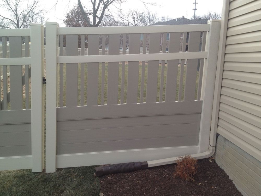 Tan and white vinyl fence and gate next to a beige house, grass in foreground.