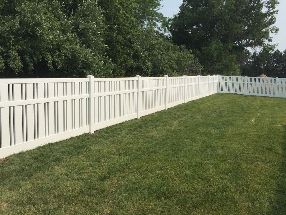 White vinyl fence surrounding a grassy yard with trees in the background.