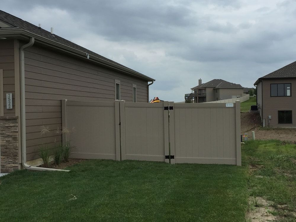 Tan vinyl fence between two houses, overcast sky.