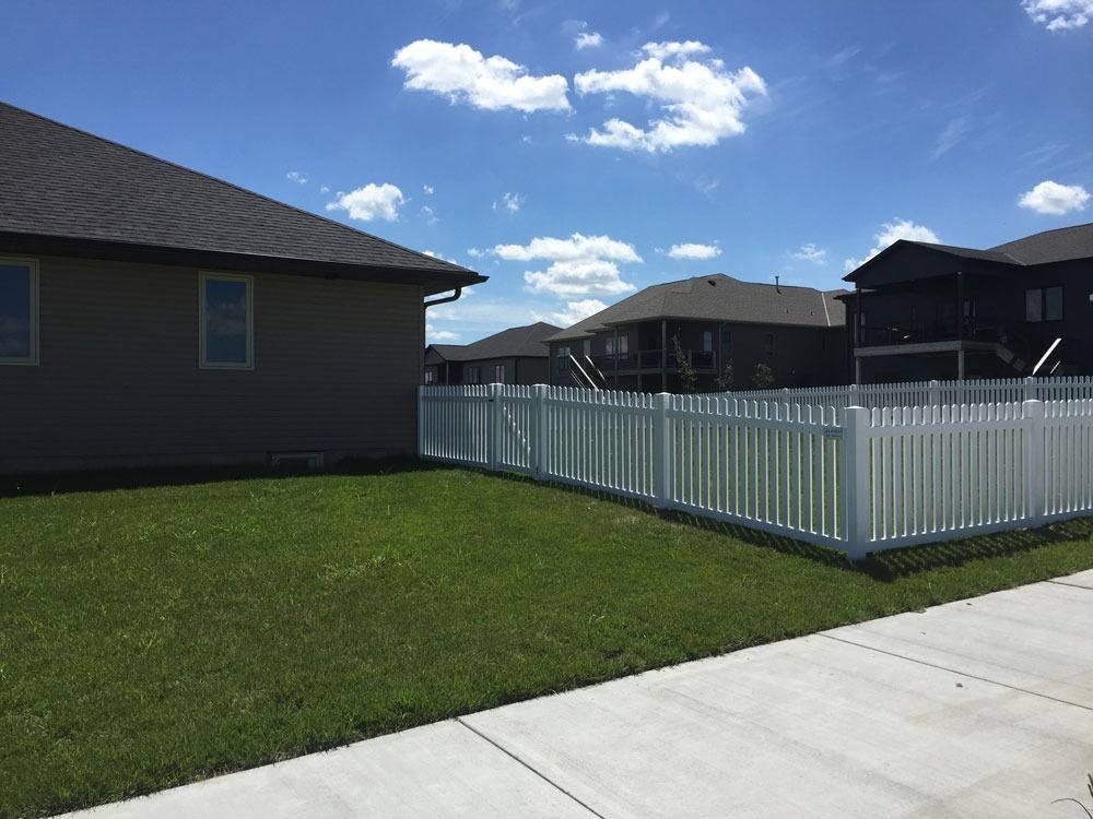 Lawn with a white picket fence bordering a building in a neighborhood. Blue sky with clouds.