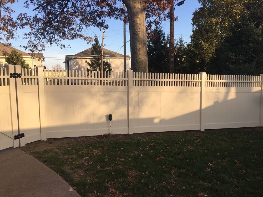 White picket fence in a yard with a gate, trees, and houses in the background.