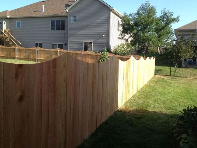 Wooden fence with a scalloped top, separating a grassy backyard from houses.
