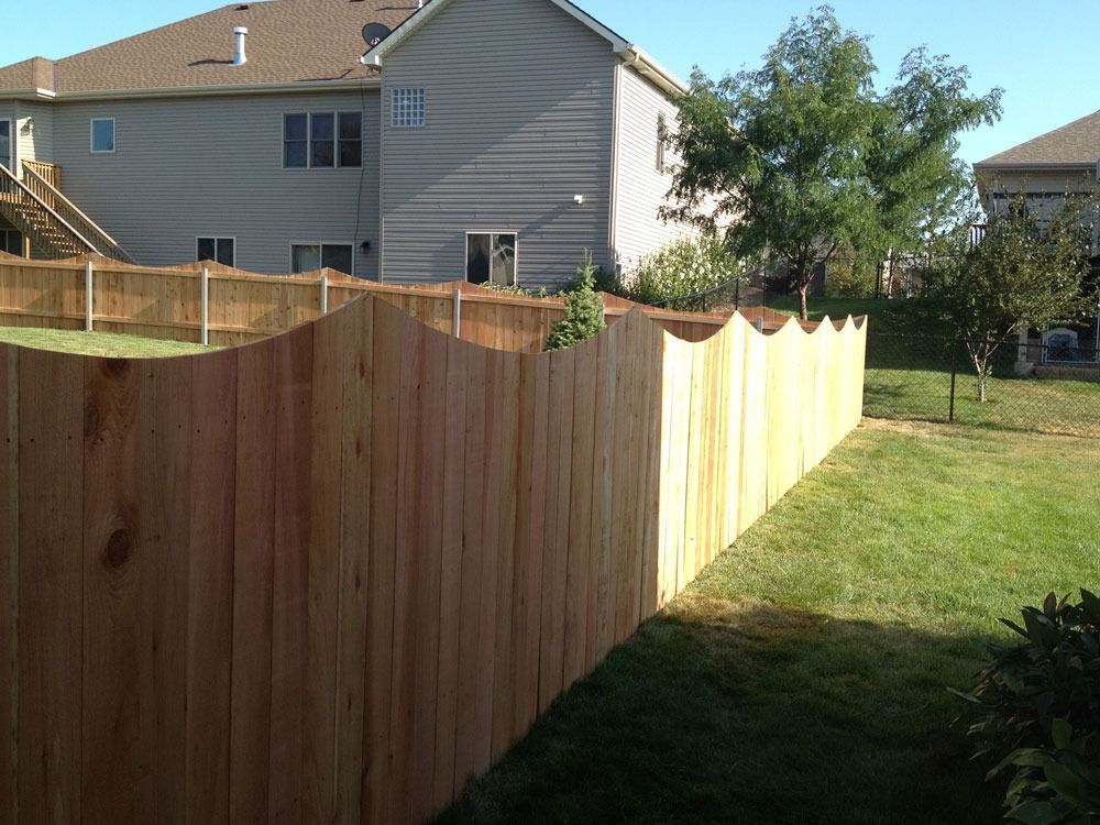 Wooden fence with a scalloped top, surrounding a grassy backyard with a two-story house.