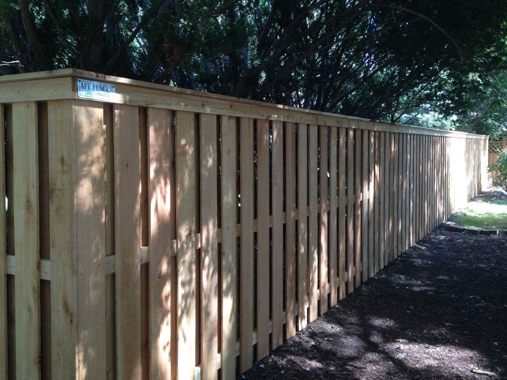 Wooden fence in a yard with vertical boards and a dark, leafy background.