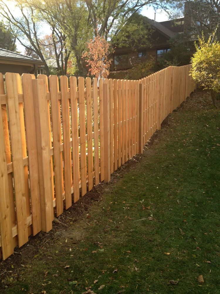 Wooden picket fence along a grassy slope, with trees and a house in the background.