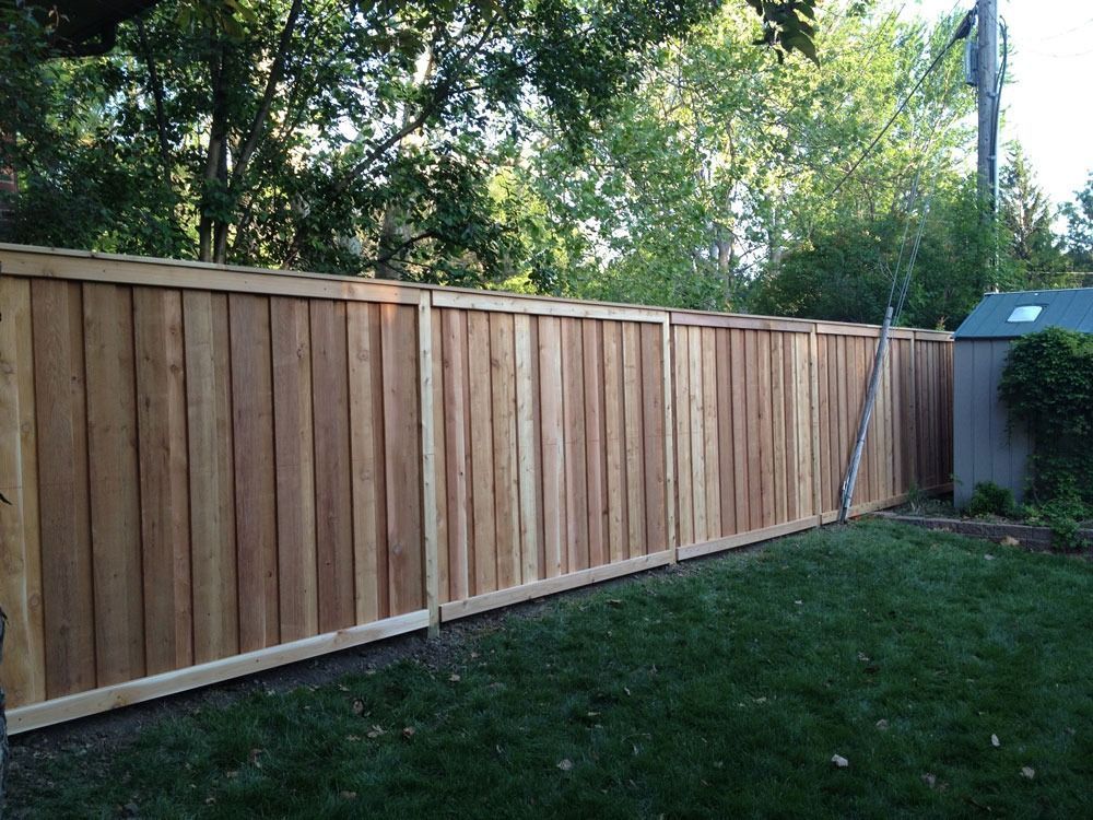 Wooden privacy fence in a backyard with green grass and trees.