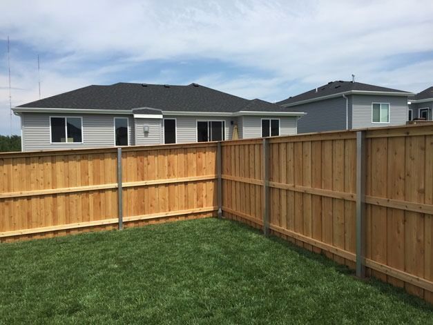 Wooden fence surrounds a grassy yard, with houses in the background under a blue sky.