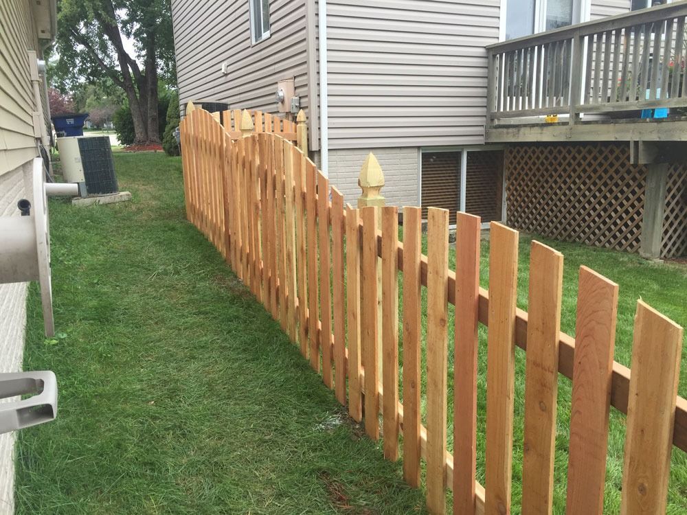 Wooden picket fence in a yard, curved, alongside a house with green grass.