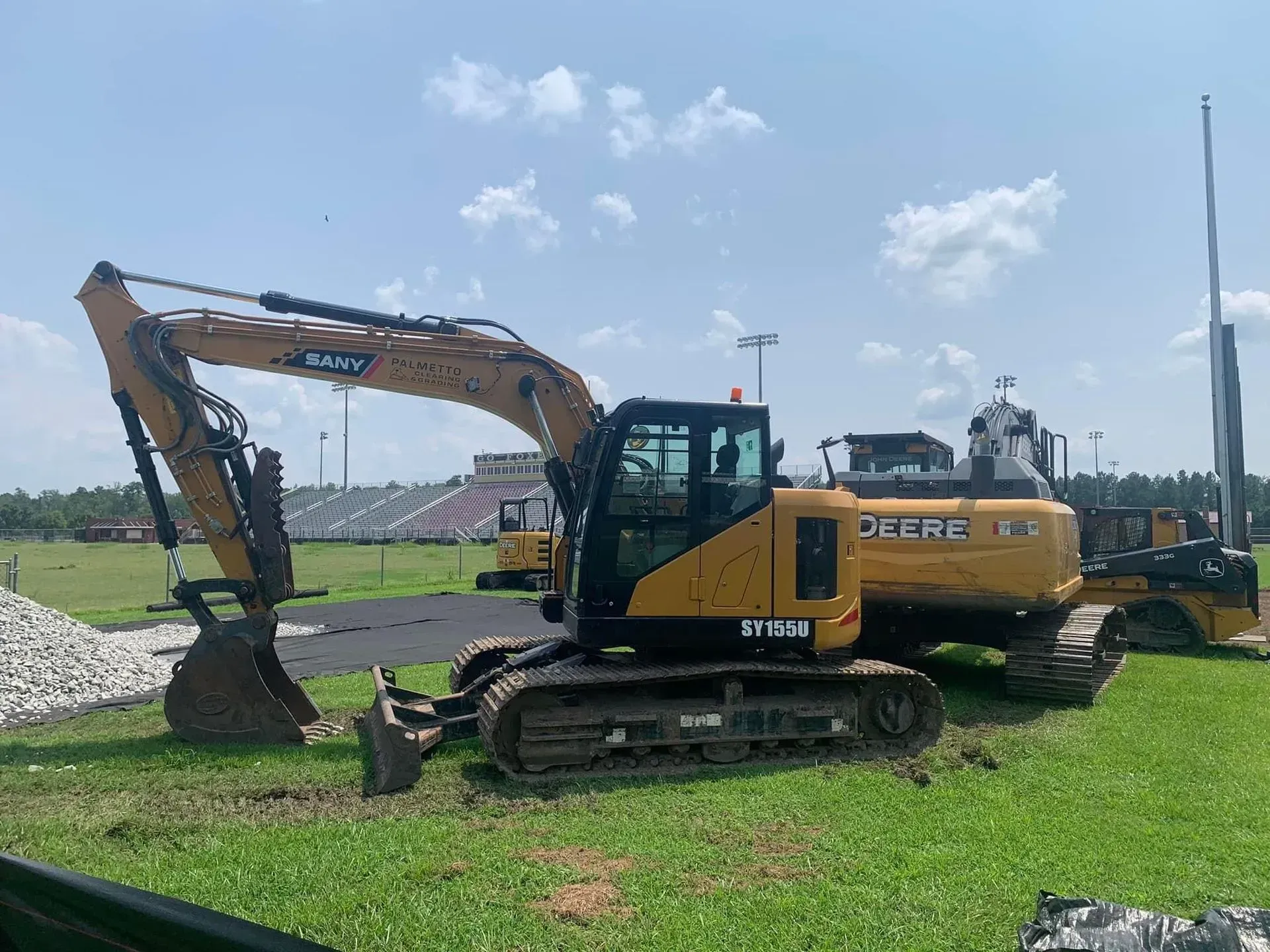 Yellow excavator on green grass with cloudy sky in background.