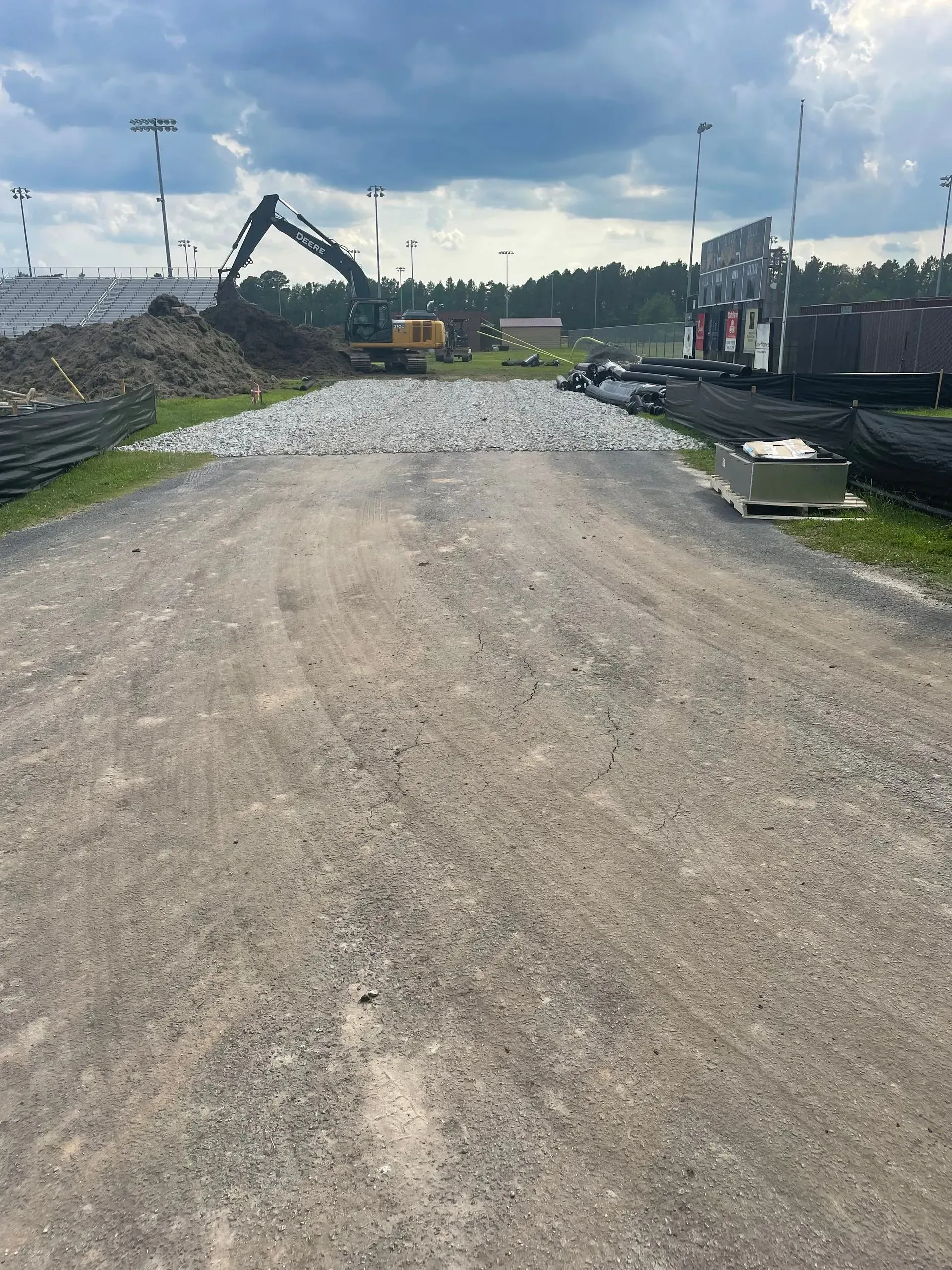 Gravel road leading towards construction site with excavator, pile of dirt, and cloudy sky.