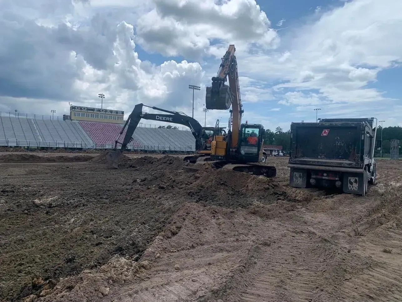 An excavator loading dirt into a dump truck at a construction site on a cloudy day.