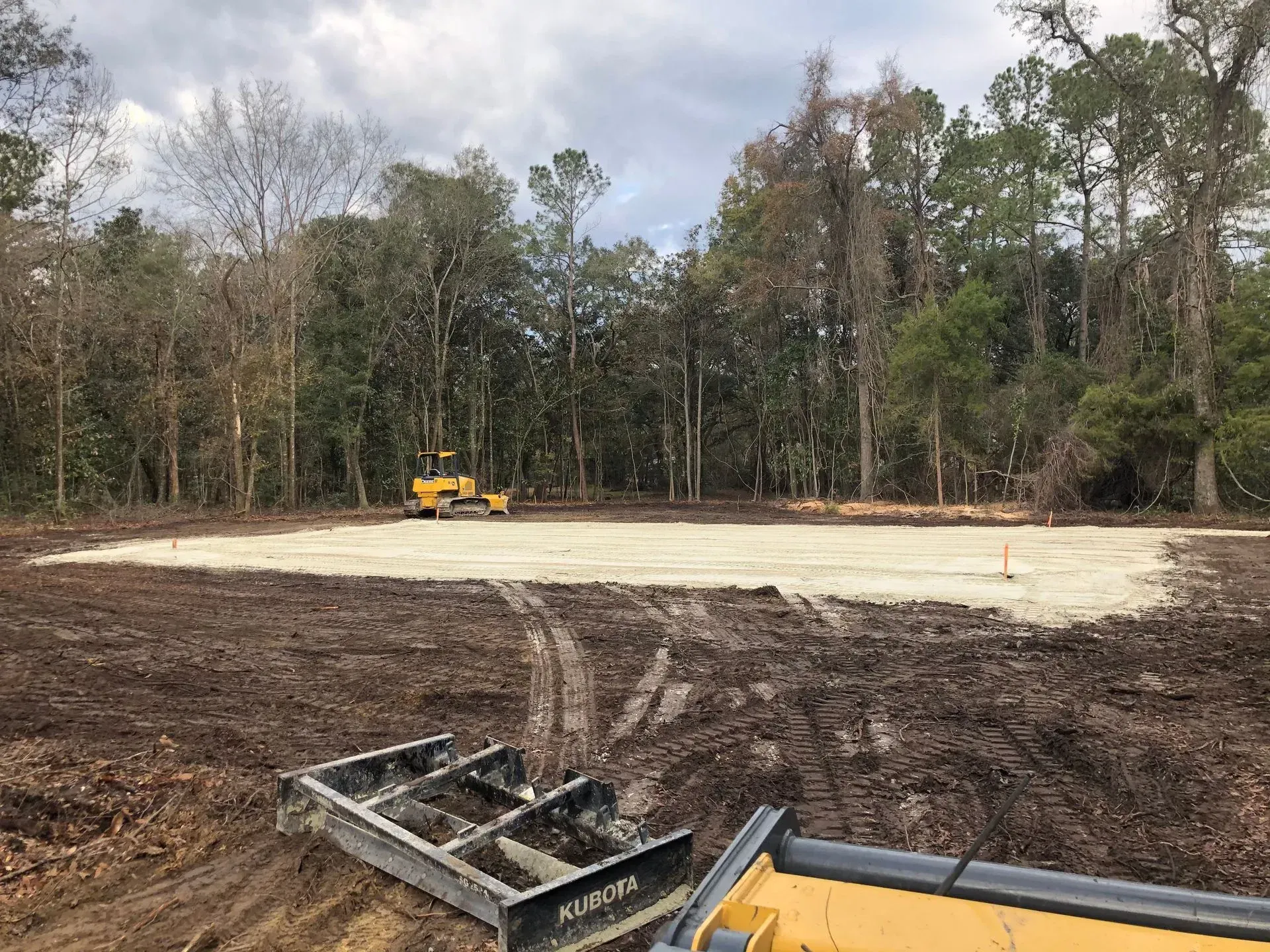 Construction site cleared, leveled, and compacted. Trees in background, Kubota leveler visible in foreground.