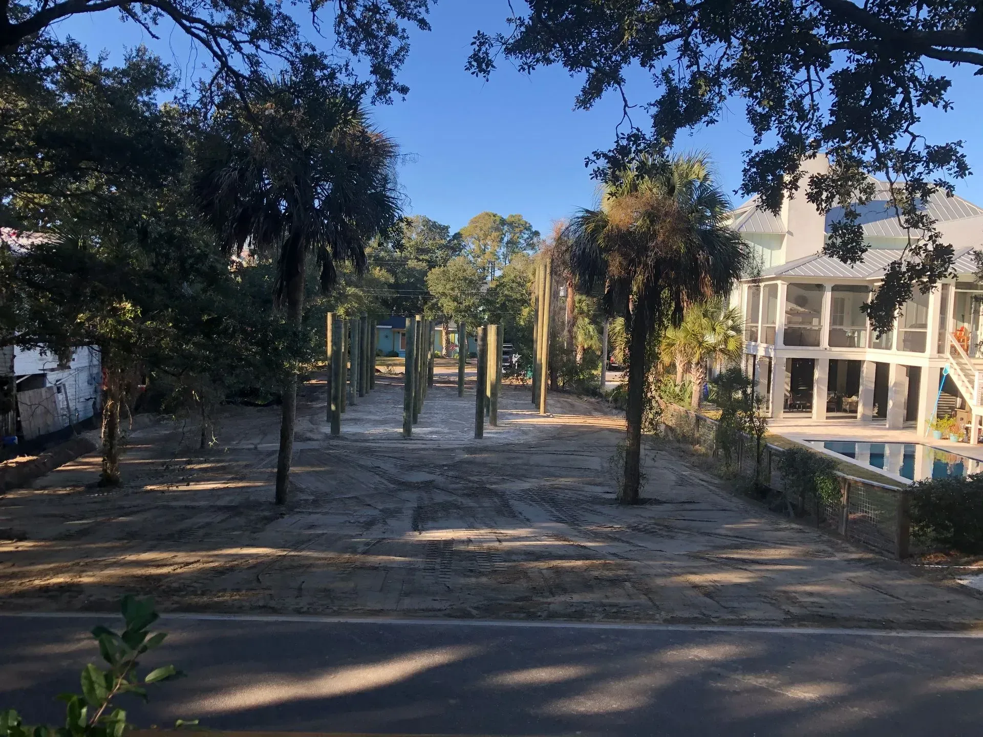 Bare, sandy lot with palm trees, road, and houses.