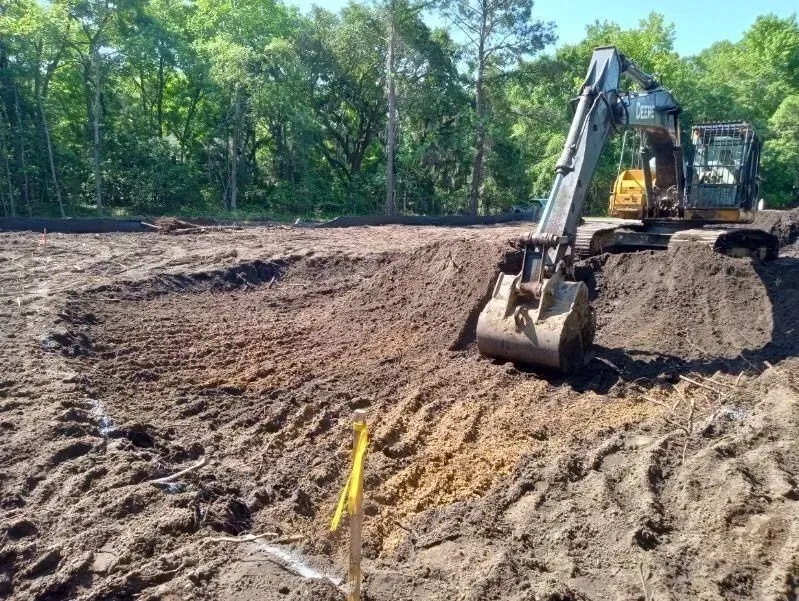 Excavator digging in dirt, marking a path. Forest in the background.