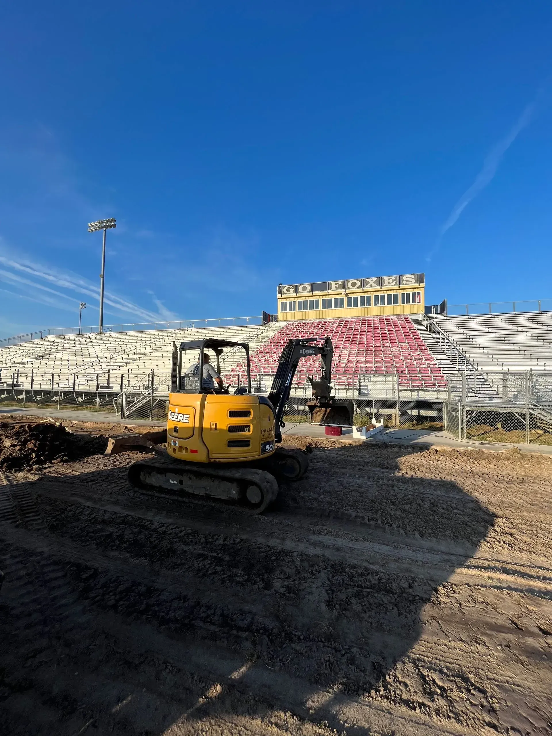Yellow excavator at a stadium construction site under a bright blue sky.