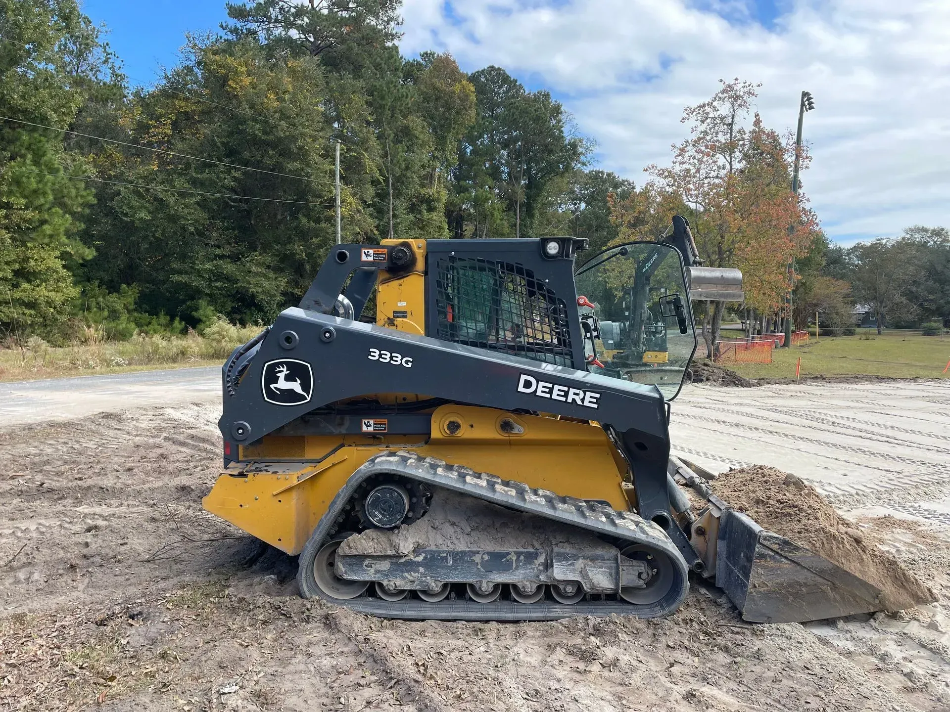 John Deere skid steer loader with tracks, yellow and black, on a gravel surface.