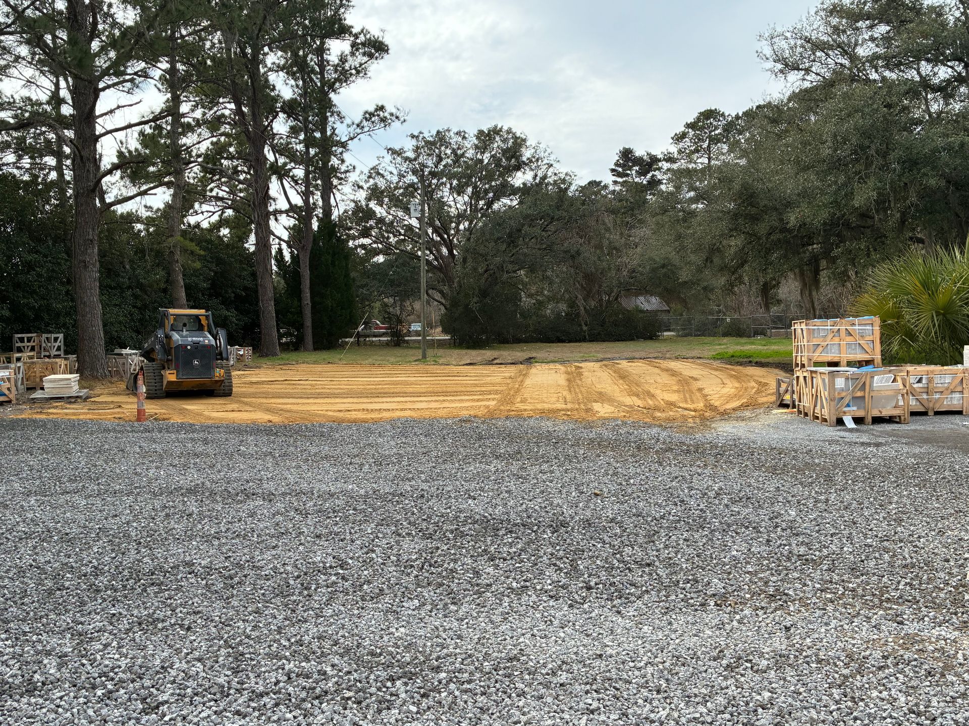 A construction site with a skid steer, a prepared dirt foundation, and wooden pallets of materials on a gravel lot.