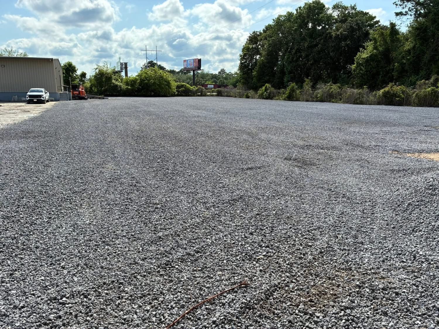 A wide, flat lot covered in grey crushed stone, with a small building and a white vehicle visible on the left.