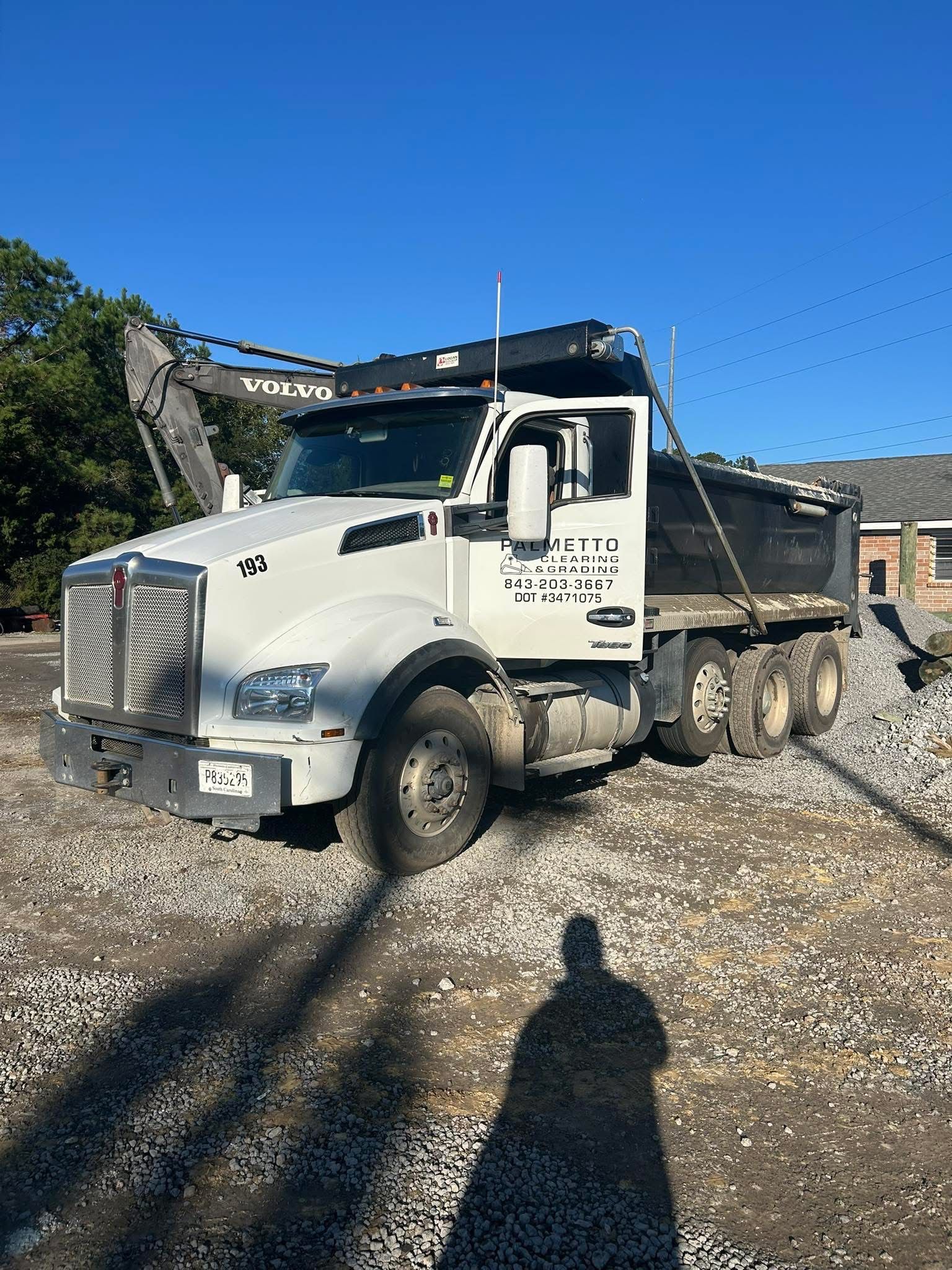 A white Kenworth dump truck parked on a gravel surface under a clear blue sky.
