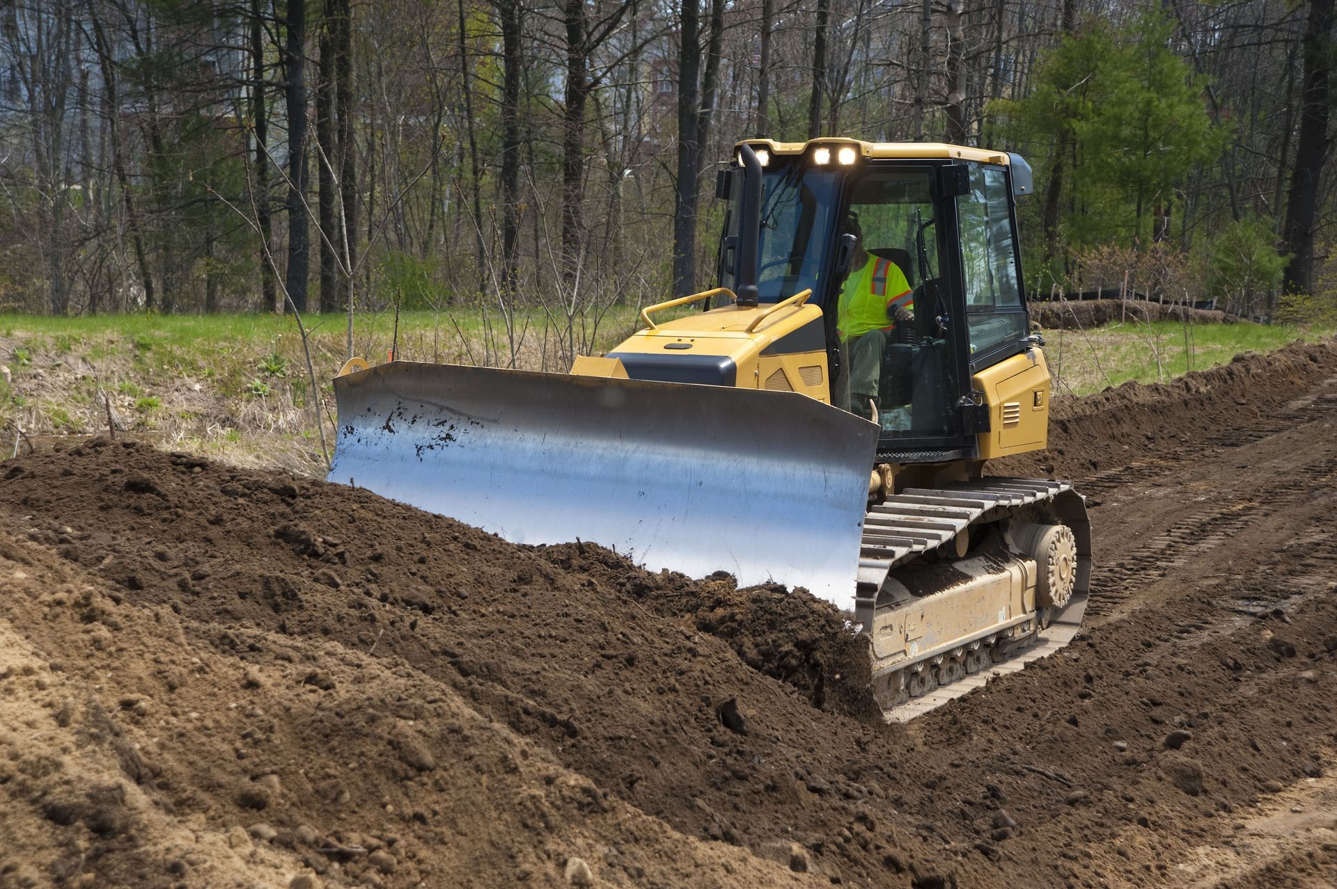 Yellow bulldozer pushes dirt, operator inside cab. Field setting, bright daylight.
