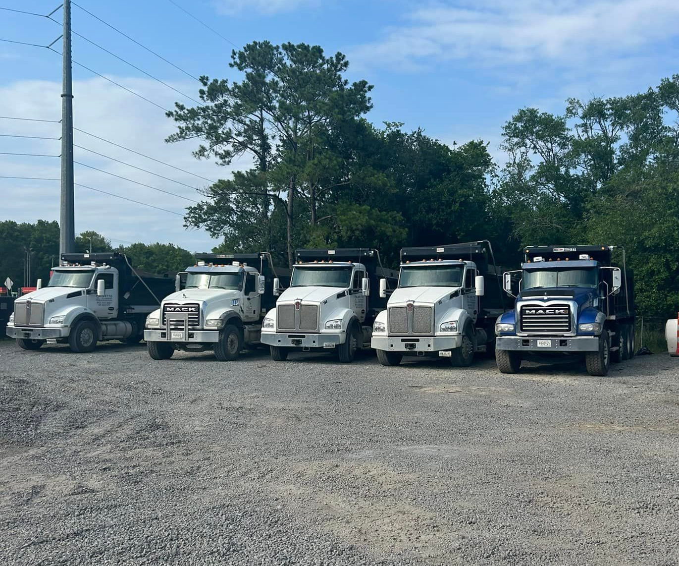View from heavy machinery. A yellow blade grading a dirt road with trees in the background.
