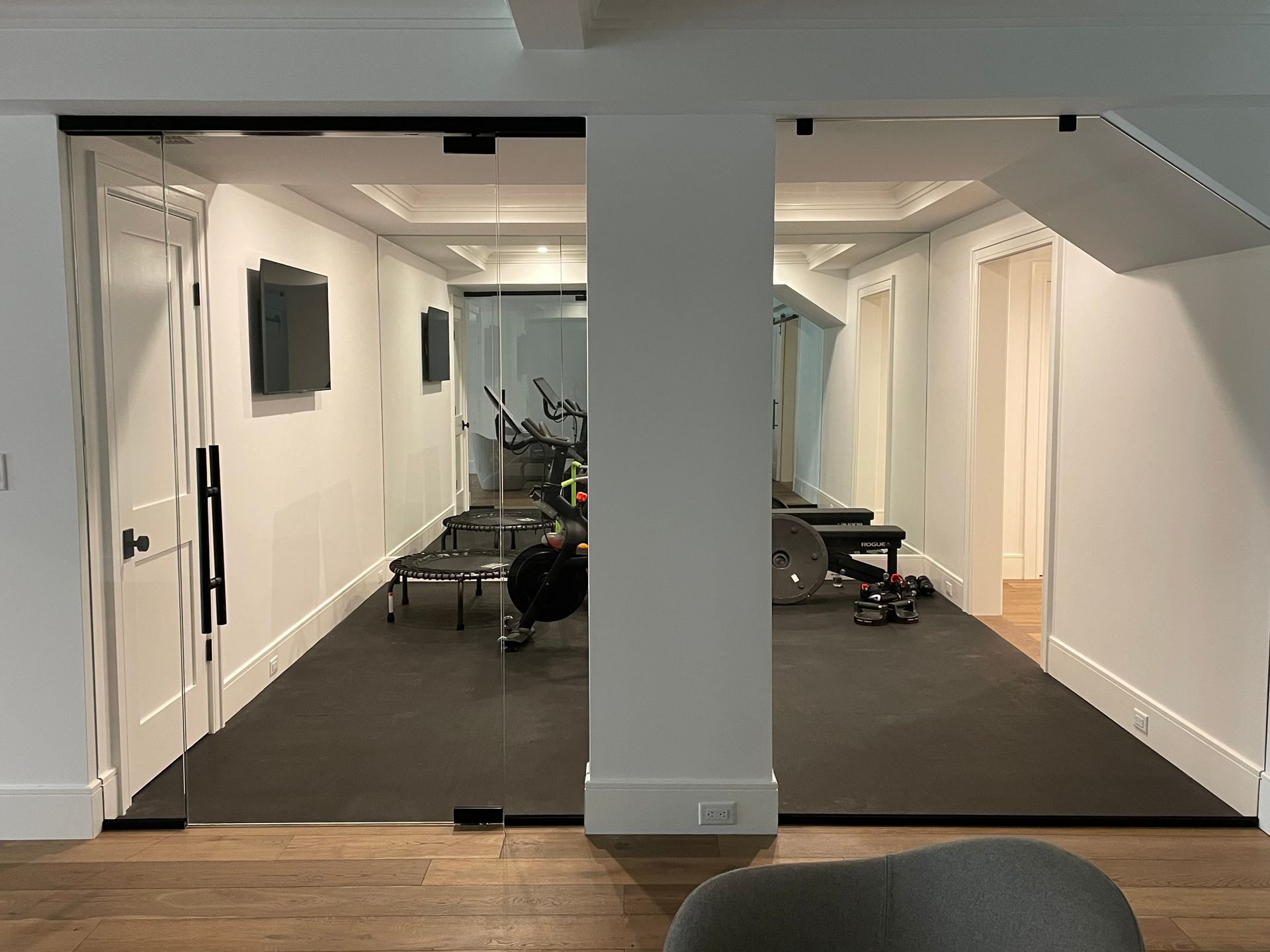 Glass-enclosed home gym with exercise equipment and mirrored walls. Flooring is black.