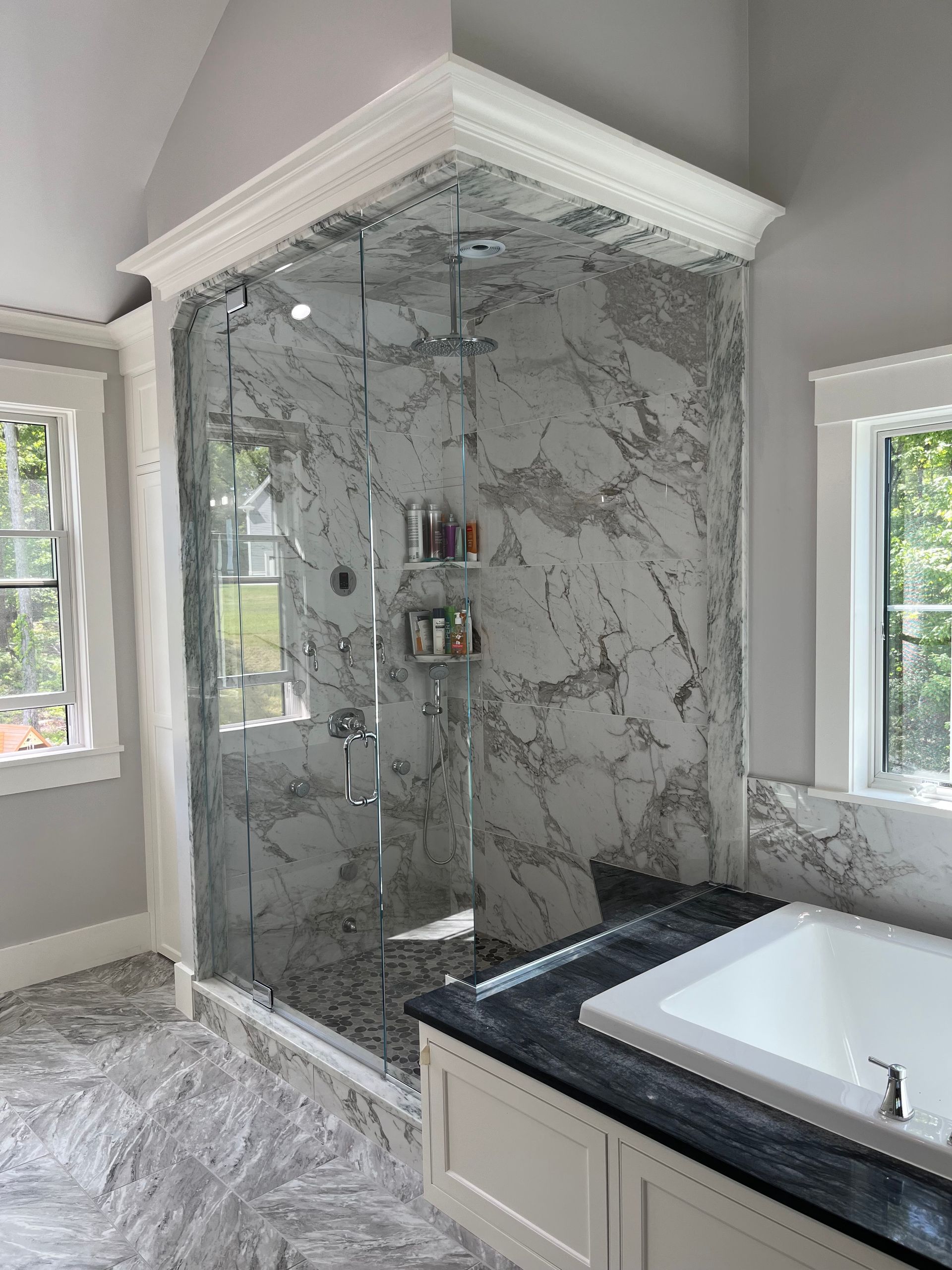 Luxurious bathroom with marble shower, glass enclosure, and white trim. Adjacent is a white bathtub with a dark countertop.